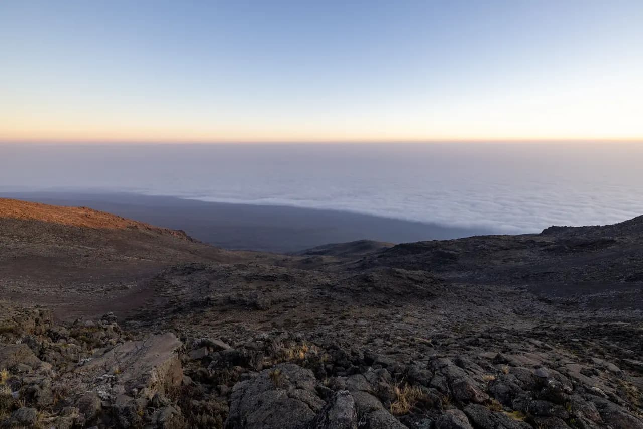 Panoramic view of volcanic landscape above clouds at sunrise from high mountain peak summit