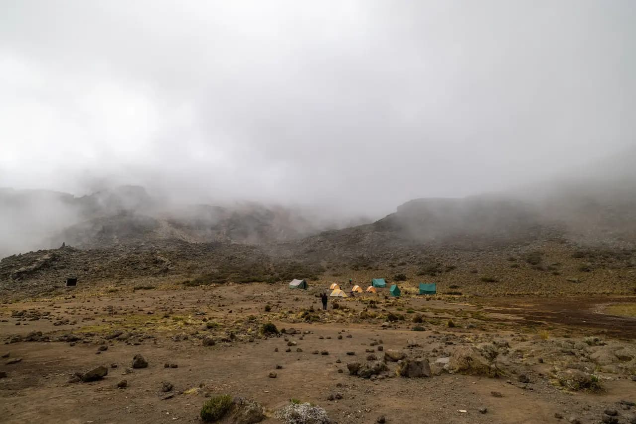 Small group of colorful camping tents pitched on a rocky mountain plateau in thick morning fog